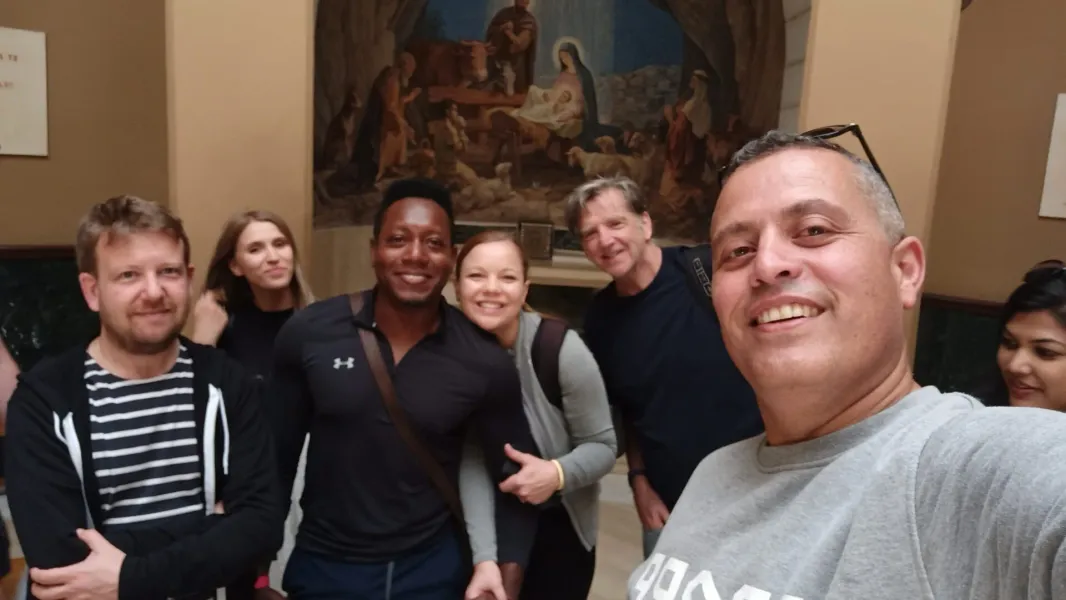 Happy tourists on a guided tour in Rome, posing for a selfie in front of a Nativity painting.