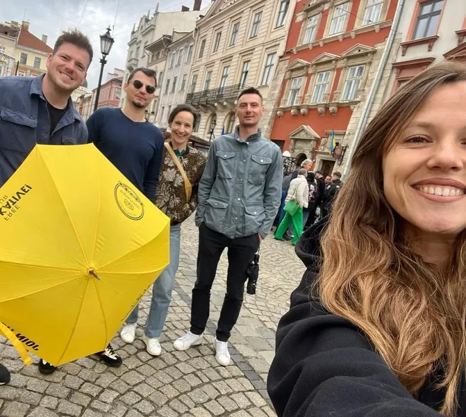 Group of five people, including a guide with a yellow Walkative umbrella, on a cobblestone street in Lviv's Old Town.