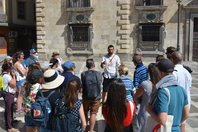 A tour guide leads a group of tourists through a historical square in Seville, Spain.