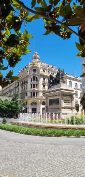A beautiful fountain and ornate building in a sunny Spanish square.