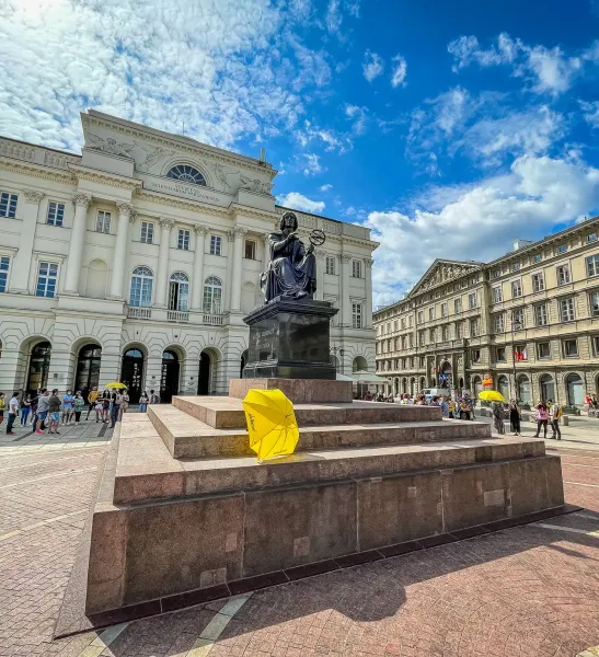 Bronze statue of Nicolaus Copernicus with an armillary sphere in Warsaw, in front of the Staszic Palace under a blue sky.