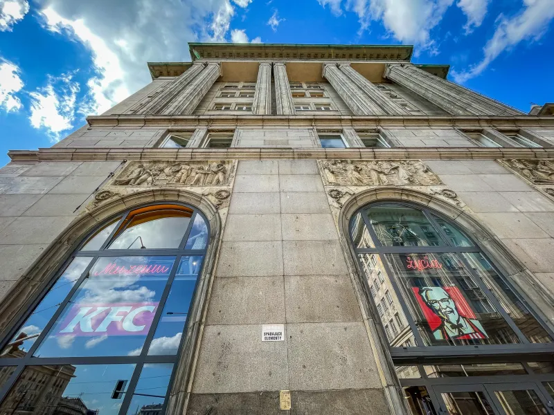 A low-angle view of a grand building in Warsaw, Poland, with a KFC restaurant visible.