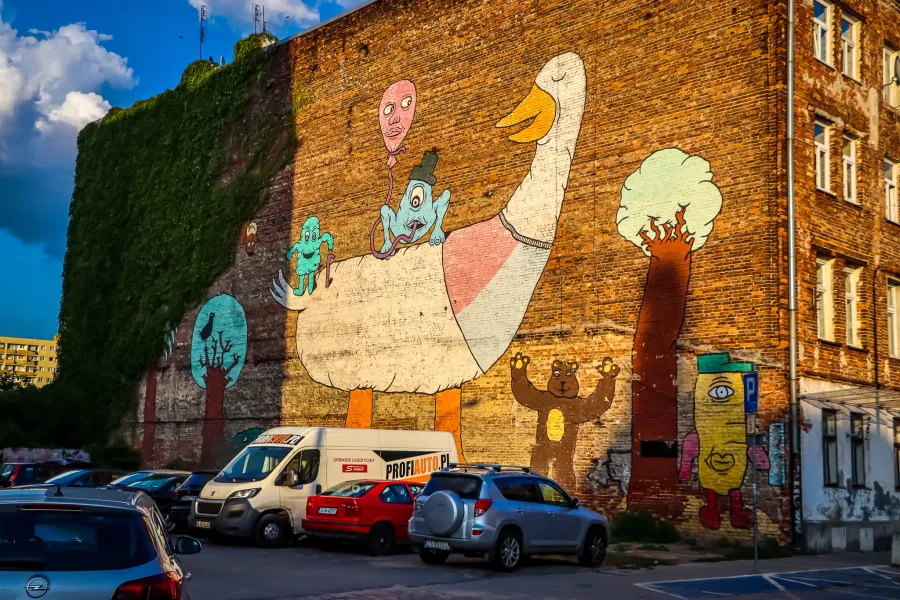 Colorful mural of a giant goose and other cartoon characters on a brick building in Warsaw.
