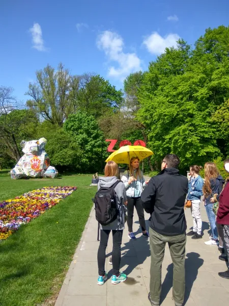 Guided tour group in Warsaw's park admiring a mosaic bear sculpture.