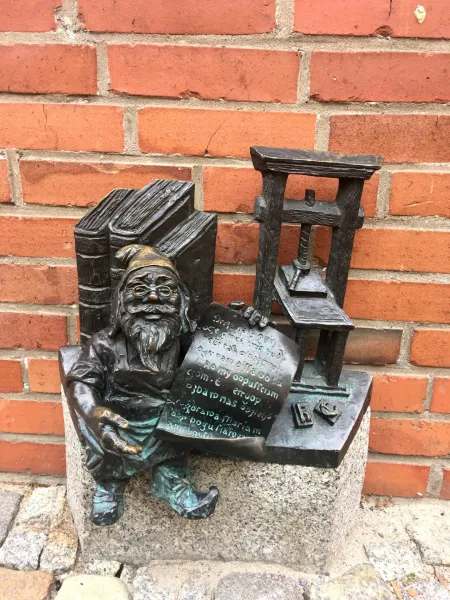 Bronze dwarf statue in Wrocław, Poland, sitting by a printing press and books.