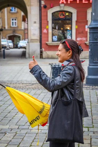 A smiling tour guide in Wroclaw gives a thumbs up, holding a yellow umbrella.