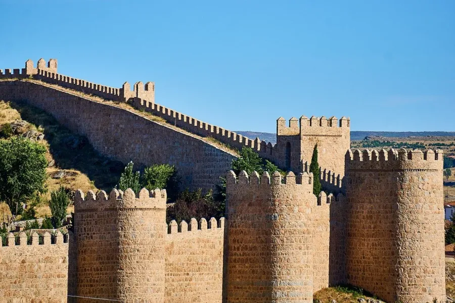 The medieval stone walls of Ávila, with their battlements and towers, on a sunny day with a clear blue sky.