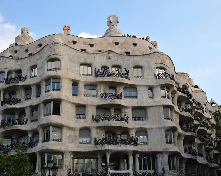 Curved stone facade of Casa Milà (La Pedrera) with ornate iron balconies under a blue sky, designed by Antoni Gaudí.