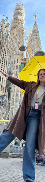 A smiling Walkative guide with a yellow umbrella in front of the Sagrada Familia in Barcelona, with its towers under const...