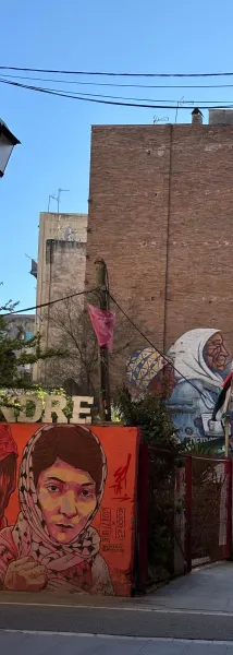 Mural of a young woman in a patterned headscarf on an orange wall, and older women murals on a brick building in Barcelona.