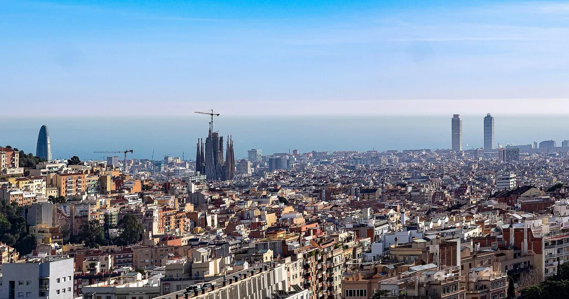 Panoramic view of Barcelona city with Sagrada Familia under construction, Agbar Tower, and two skyscrapers by the sea.