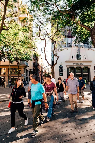 Group of people walking on a sunny street past El Molino theatre with a windmill on its facade in Barcelona.