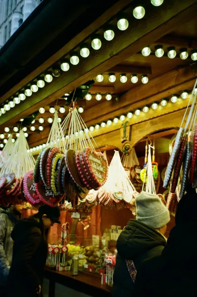Hanging gingerbread heart cookies with icing decorations and various sweets at a festive market stall, with people browsing.