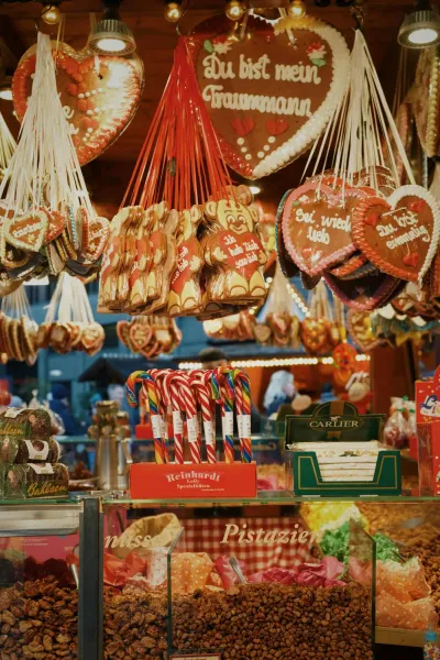 A stall at a Christmas market selling gingerbread hearts, candy canes, and roasted nuts under warm lights.