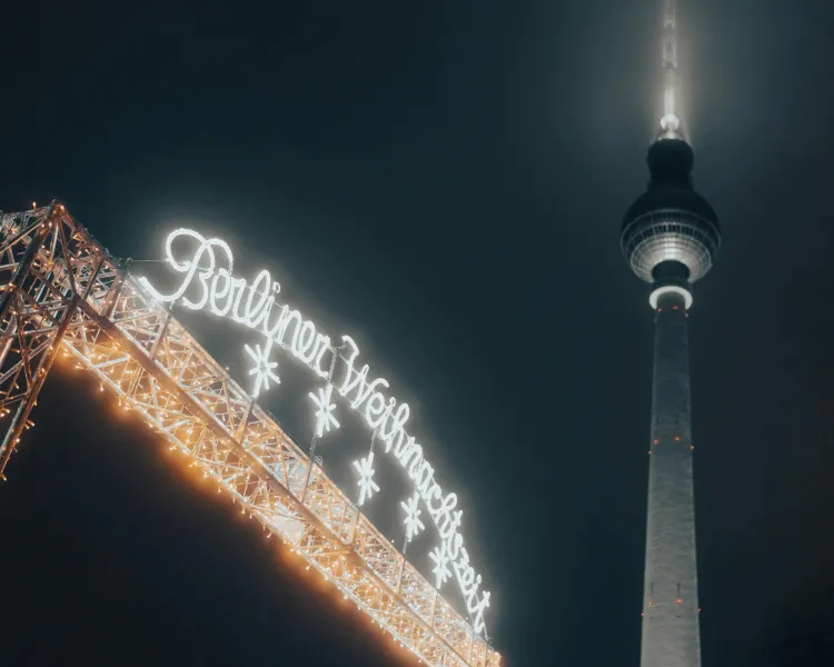 Illuminated 'Berliner Weihnachtszeit' sign and a section of the Berlin TV Tower against a dark night sky.