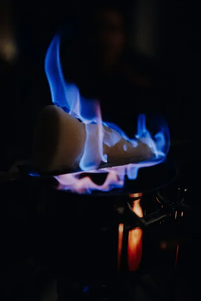 Sugar cone with blue flames burning over a dark pot, illuminating the foreground against a dark background.
