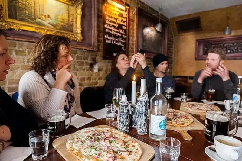 A group of people sitting at a long table in a cozy Berlin restaurant, with Flammkuchen and drinks in front of them.