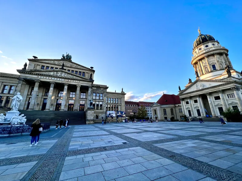 View of Gendarmenmarkt in Berlin with the Konzerthaus (left) and Deutscher Dom (right) under a clear blue sky.