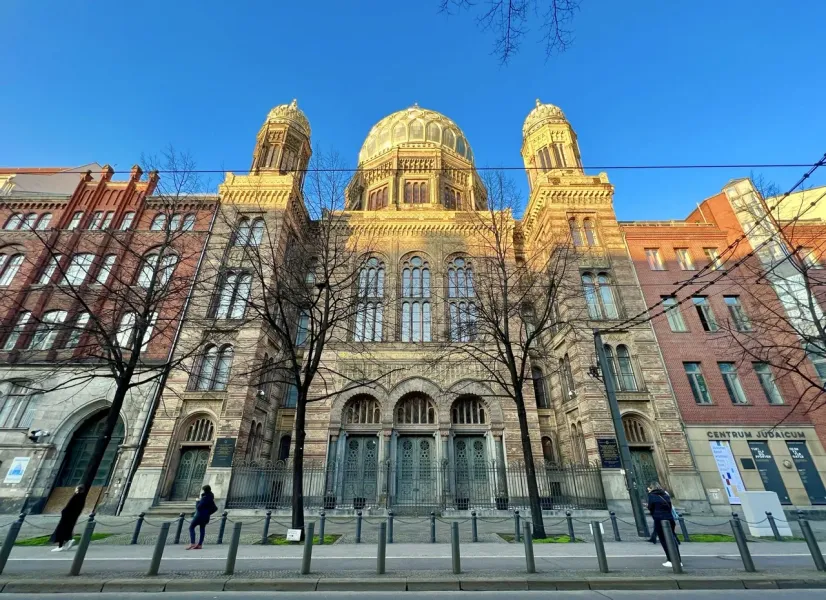 The ornate facade of the New Synagogue in Berlin on a sunny day, viewed from across the street through bare trees.