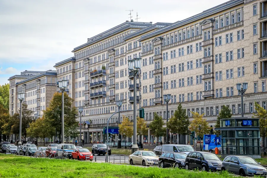 Large multi-story apartment buildings with streetlights, parked cars, trees, and a U-Bahn station entrance in Berlin.