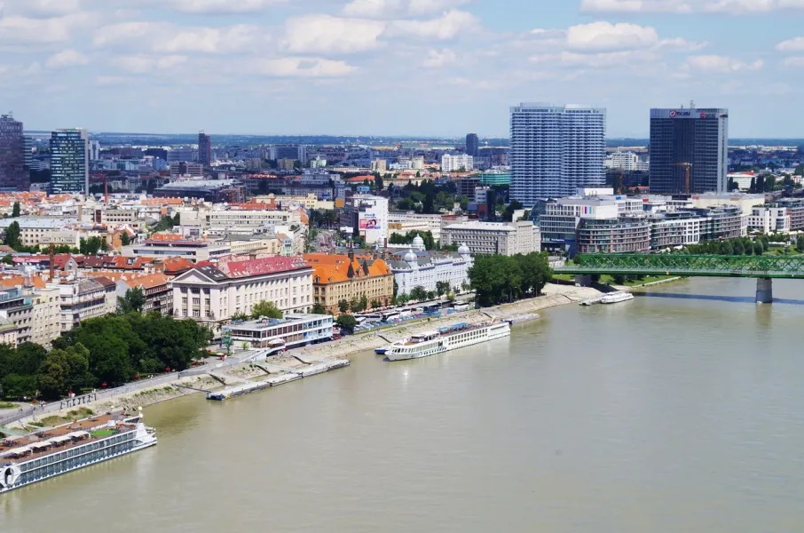 Aerial view of Bratislava cityscape along the Danube River, featuring modern skyscrapers, historic buildings, and a green ...