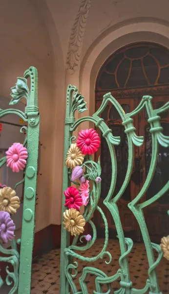 Ornate green Art Nouveau metal gate with colorful pink, gold, and purple floral decorations, in front of an arched wooden ...