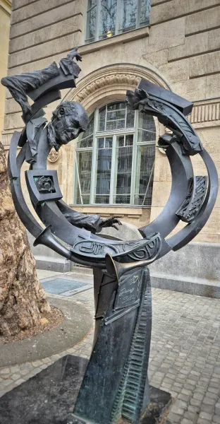 Bronze sculpture in Budapest featuring a man's head, hands, trumpets, piano keys, and abstract forms in a circular design.