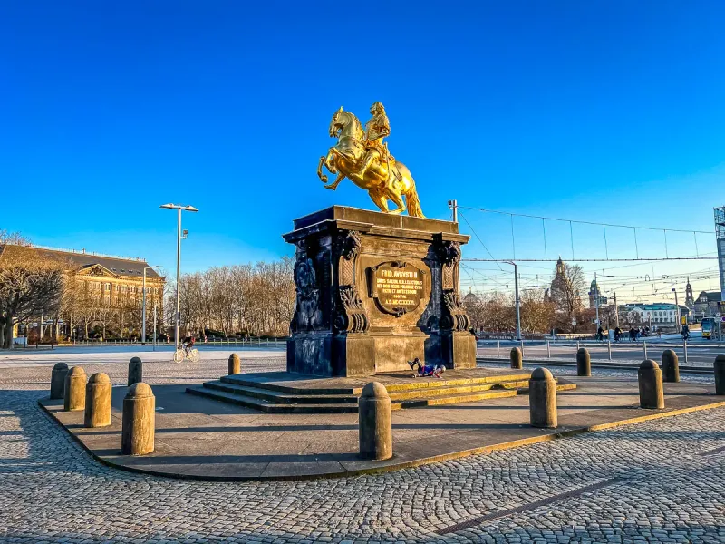 Golden equestrian statue of August the Strong on a dark pedestal in a cobblestone square, Dresden.