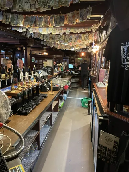 Interior of a traditional Glasgow pub with a long wooden bar, many beer taps, and banknotes from various countries strung ...