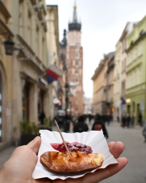 Hand holding grilled oscypek cheese with jam. St. Mary's Basilica in Kraków is blurred in the background.