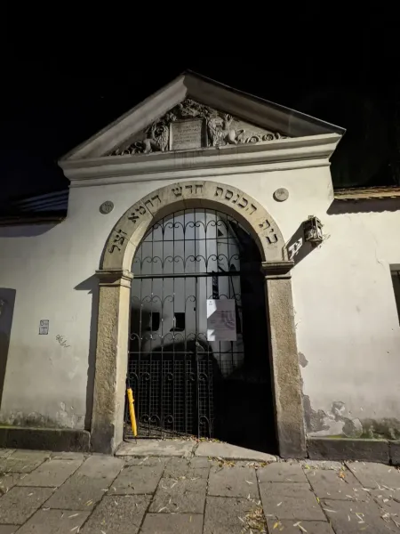 Stone entrance to the Isaak Synagogue in Krakow's Kazimierz district at night, with Hebrew script over an arched gate.