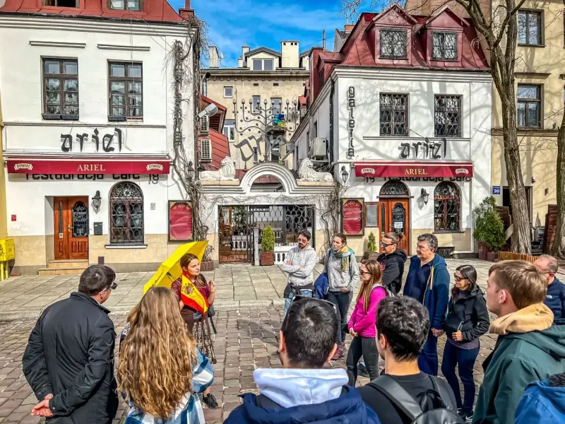 A tour group listens to a guide with a yellow umbrella on Szeroka Street in Krakow's Kazimierz district.