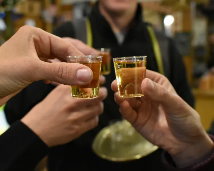 Close-up of three hands toasting with small tasting glasses of amber liquid in Krakow.