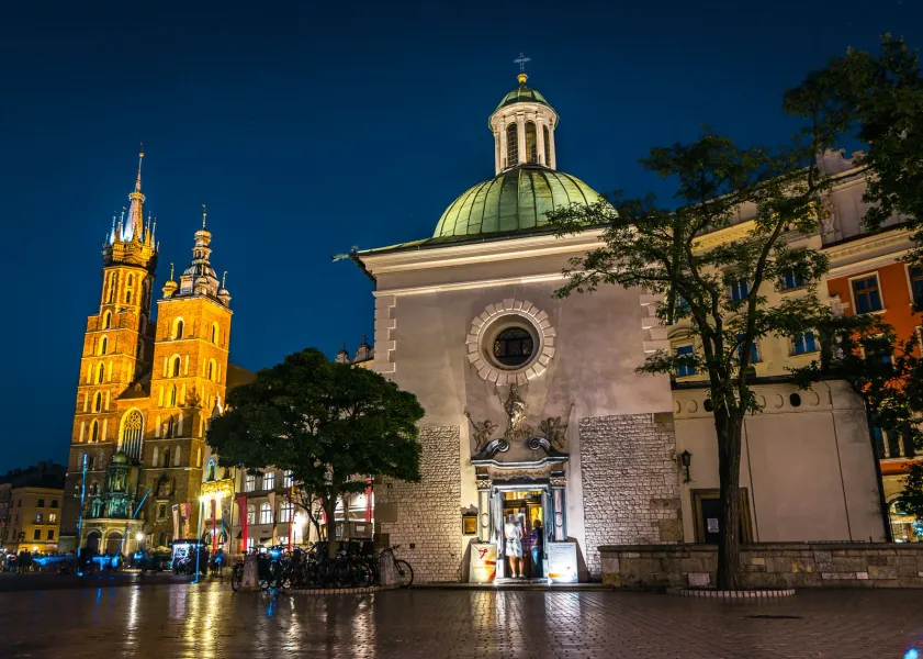 St. Mary's Basilica and St. Adalbert's Church lit up at night on Krakow's Main Market Square with wet cobblestones.