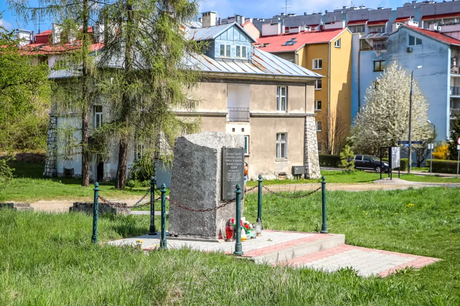 A stone memorial in a grassy area in front of the historic Grey House at the former Płaszów camp site in Krakow.