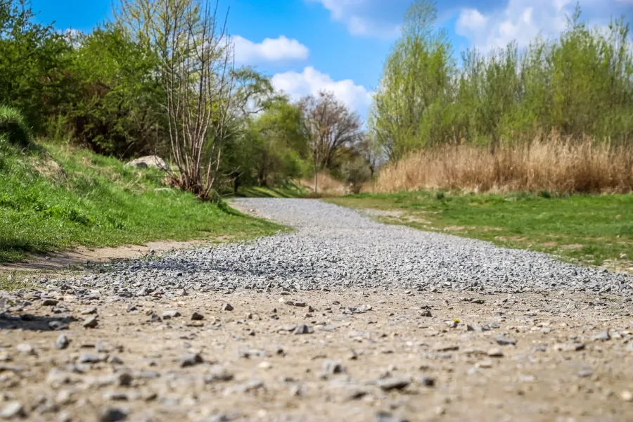 Gravel path winding through green grass and trees under a blue sky, indicating the memorial grounds of KL Plaszow.