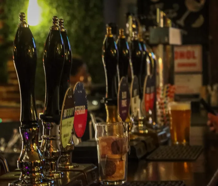 A row of shiny black beer taps on a wooden bar in a dimly lit Krakow pub. A pint glass sits in the background.