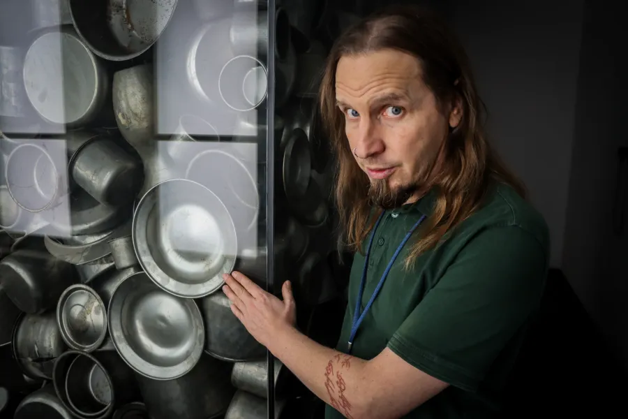 The guide stands beside a glass display filled with reproductions of metal pots like those produced by Schindler's Factory...