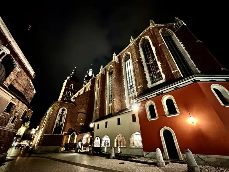 St. Mary's Basilica in Krakow at night, showing its brick facade, gothic windows, and two towers under a dark sky.