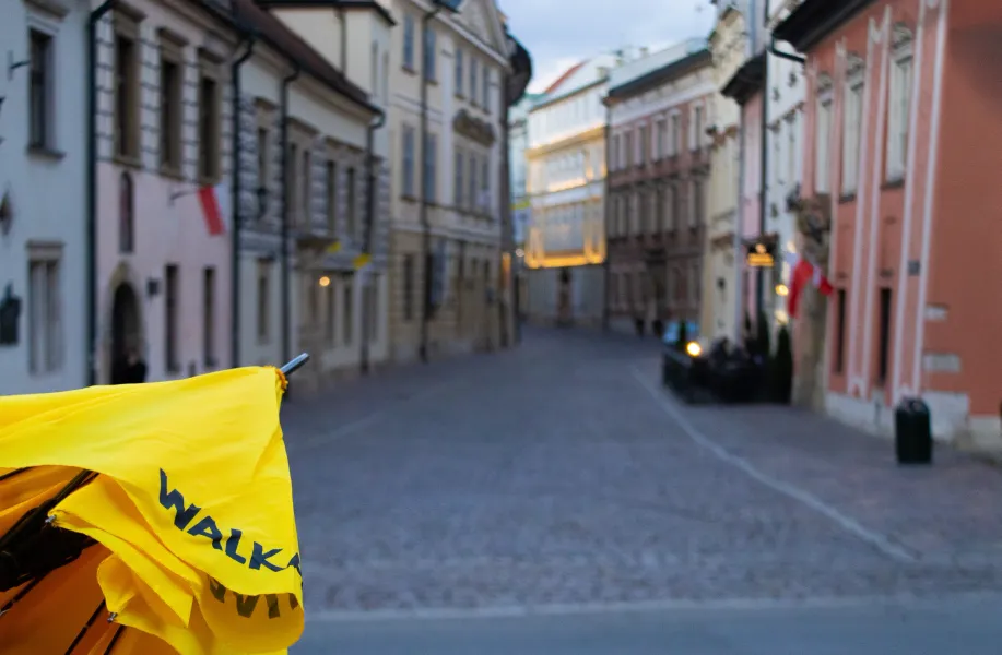 A yellow Walkative tour umbrella in the foreground, with a blurred view of a cobblestone street in Krakow's Old Town.