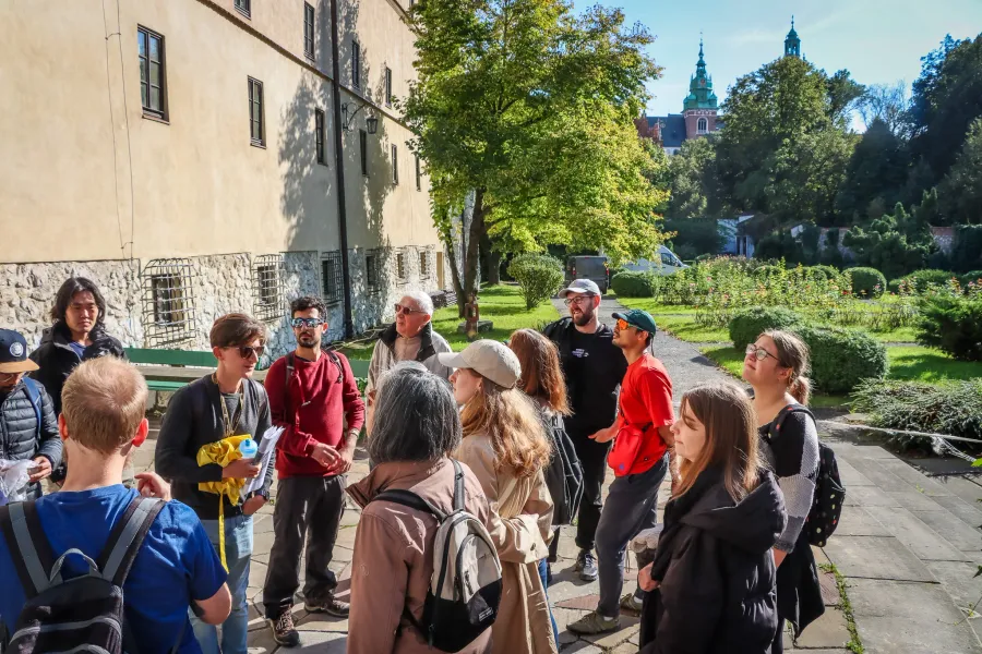A group of tourists listening to a guide on Wawel Hill in Krakow, with the cathedral towers visible in the background.