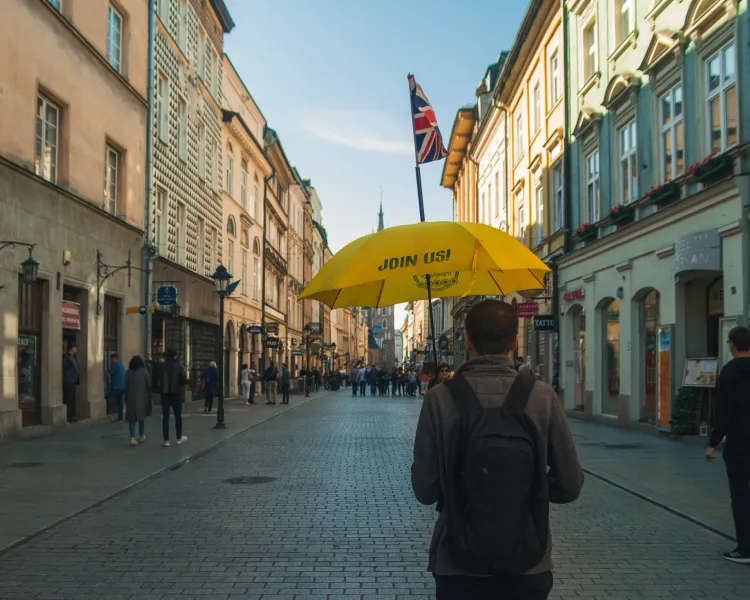 A tour guide holds a yellow umbrella on a historic cobblestone street in Krakow, leading a group toward a church tower.