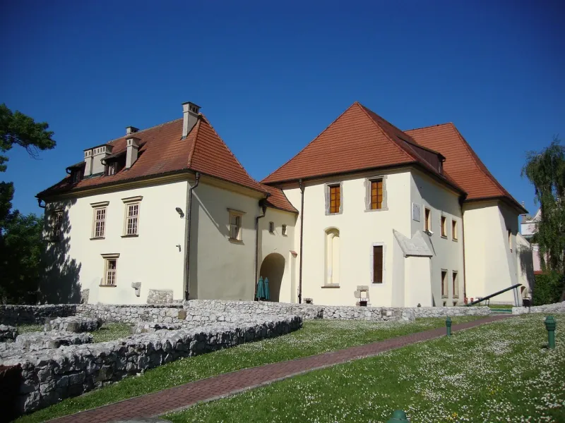 Historic white buildings with red tile roofs at the Wieliczka Salt Mine, with old stone foundations on a lawn in front.