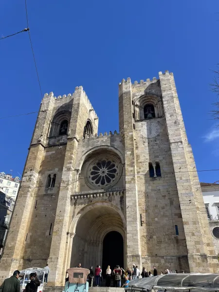 The facade of Lisbon Cathedral (Sé de Lisboa) with two square towers, a central rose window, and an arched entrance under ...