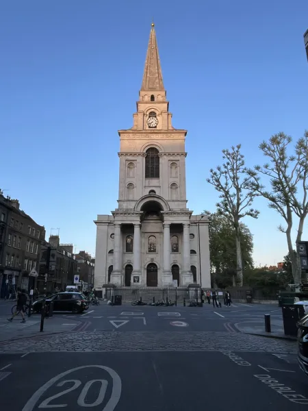 Christ Church Spitalfields seen from a cobbled street corner, its stone facade and steeple lit by the setting sun.