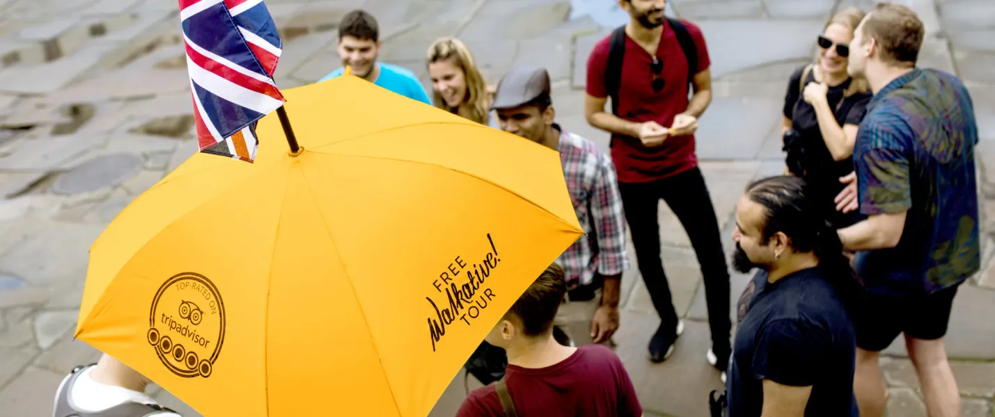 A diverse group of people listening to a tour guide holding a yellow Walkative umbrella with a small Union Jack flag.