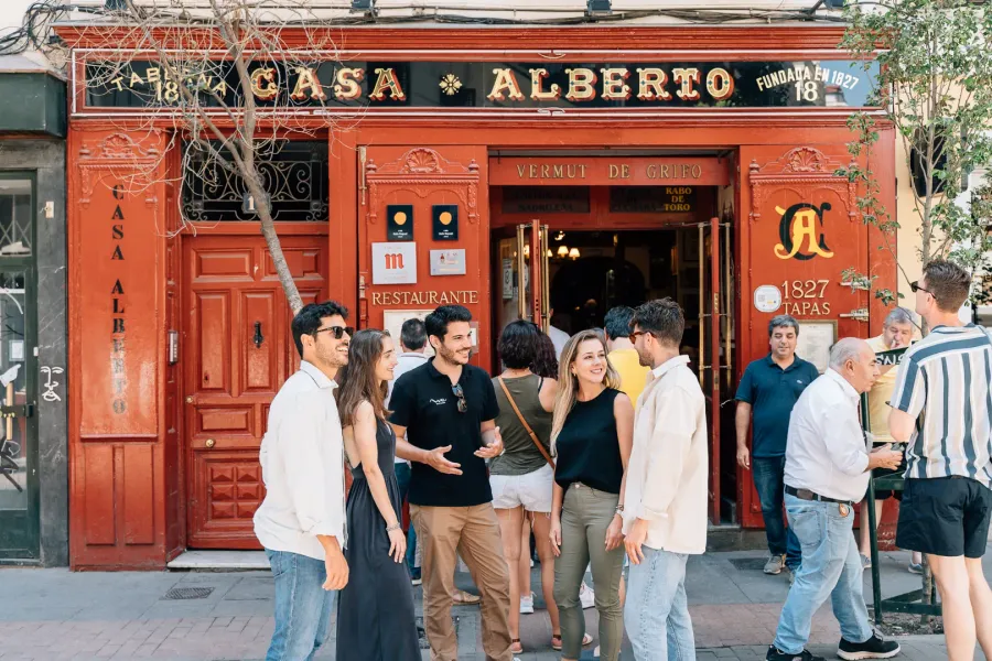 A tour guide talks to tourists in front of the red facade of the historic Casa Alberto tavern in Madrid.