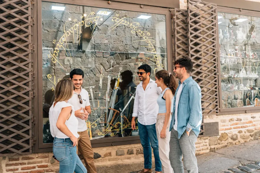 A group of five young adults talking in front of a shop with gold script on its display window.