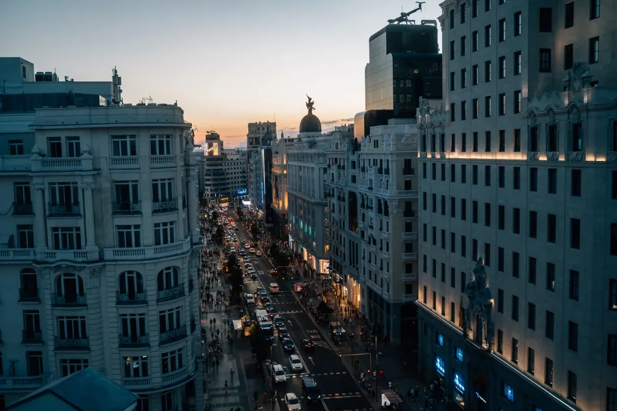An elevated view of Madrid's busy Gran Vía street at sunset, bustling with cars and pedestrians on the sidewalks.