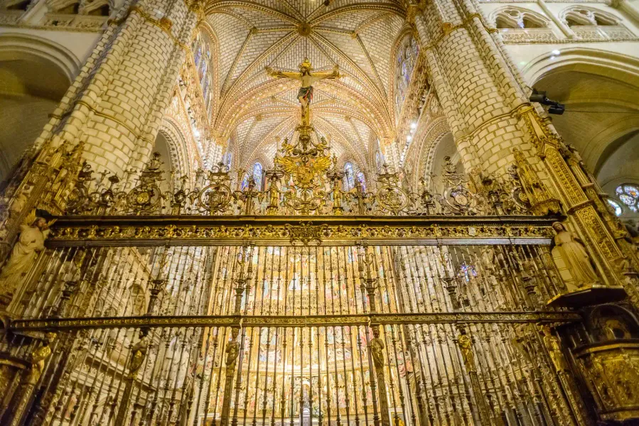 Ornate golden chancel screen below a crucifix and high vaulted ceiling inside the Toledo Cathedral, Spain.
